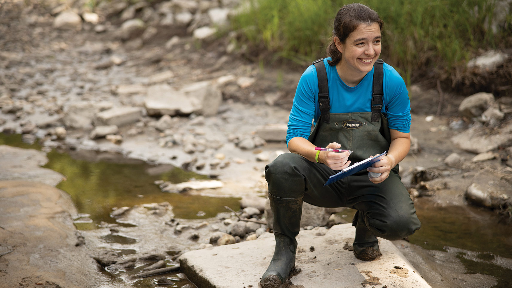 student in waders kneeling in stream bed