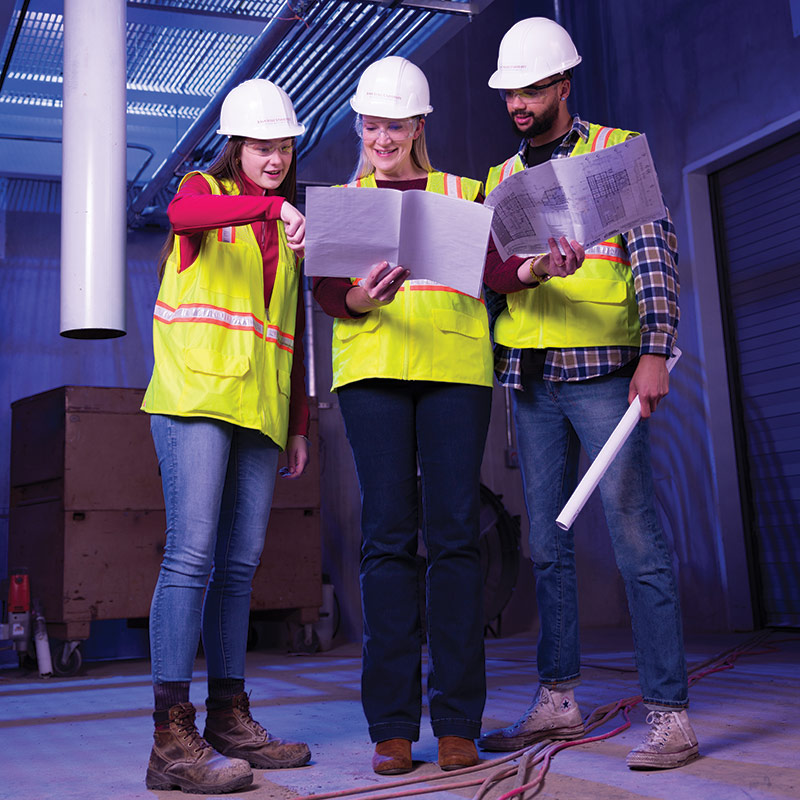 students and faculty member reviewing blueprints at construction site