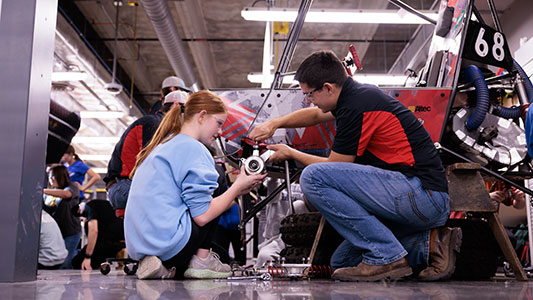 students work together, in shop setting, on Baja team vehicle