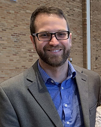 Mechanical engineering associate professor Travis Sippel smiles for the camera. He's wearing a grey suite coat and a blue collared shirt.